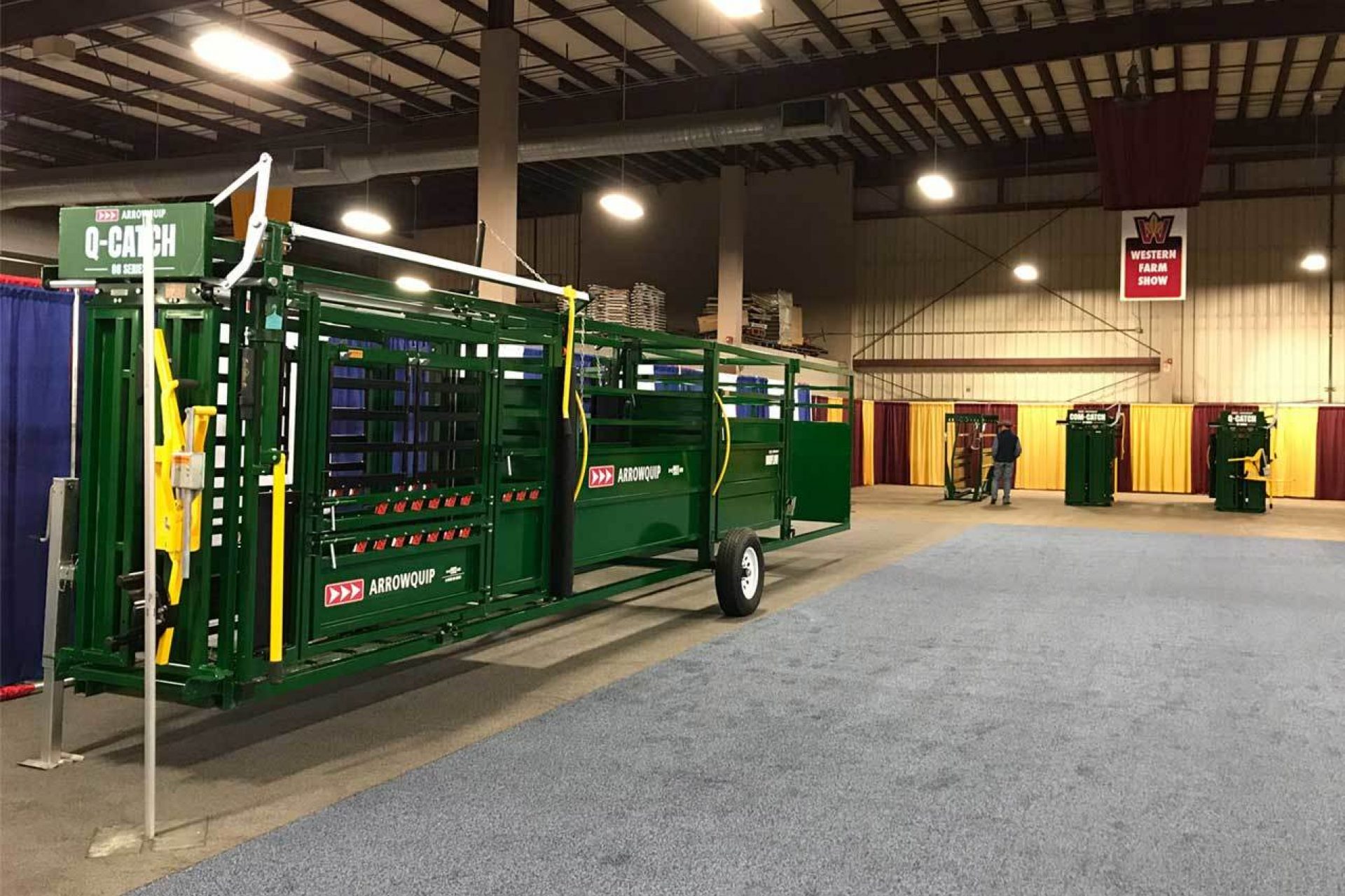 Q-Catch 86 Series portable cattle chute, alley, and tub on display at a trade show with other Arrowquip Cattle Chutes in the background