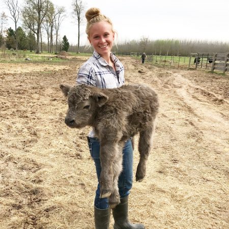 Molly Brown, female cattle rancher, holding brown highland calf